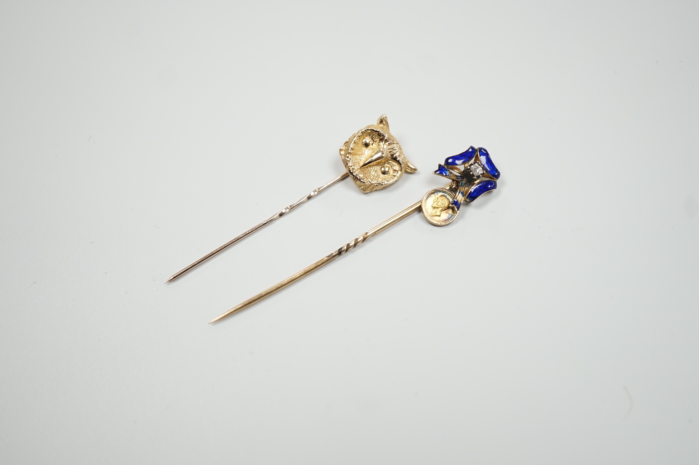 An early 20th century yellow metal enamel and diamond set ribbon bow stick pin, hung with a miniature medallion, 63mm and a later 9ct gold stick pin, gross 5.2 grams.